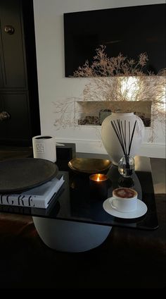 a glass table topped with a vase filled with flowers next to a book and candle