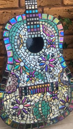 a guitar made out of stained glass and mosaic tiles, sitting against a brick wall