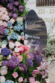 a welcome sign surrounded by colorful flowers in front of a wall with the words welcome to the wedding of dan thanh and minh hoa