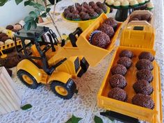 a table topped with lots of cupcakes next to a yellow truck filled with chocolate frosting