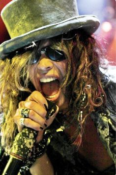 a man in a top hat and sunglasses singing into a microphone with his mouth open