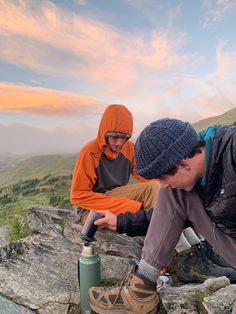 two people sitting on top of a rock next to a fire hydrant in the mountains