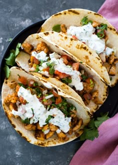 three tacos on a plate with sour cream and cilantro garnish