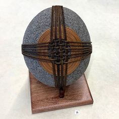 a sculpture made out of wood and stone on top of a wooden stand with a ball in the center