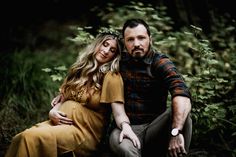 a man and woman sitting next to each other on the ground in front of trees