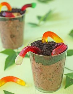 three glasses filled with dirt and gummy bears on top of a table next to leaves