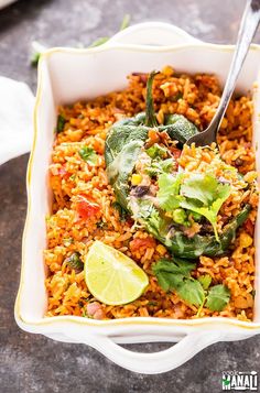 a white bowl filled with rice and vegetables next to a lime wedge on the side