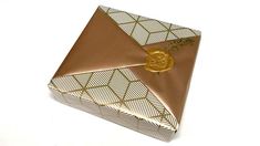 an origami box with a gold rose on it sitting on a white surface