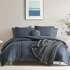 a bed with blue comforters and pillows in a room next to a potted plant