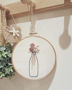 a hand embroidery project with flowers in a mason jar hanging from a hook on a wall