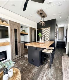 a kitchen and living room in a mobile home with wood flooring, black cabinets, white walls, and ceiling fan