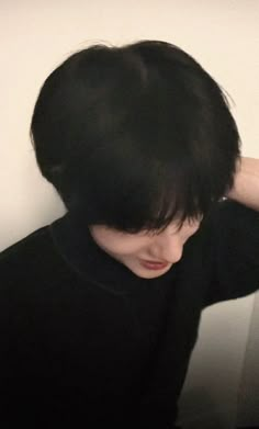 a young man with black hair wearing a black shirt and holding his head to the side