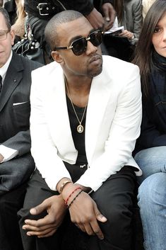 a man sitting in front of a crowd wearing sunglasses and a white suit with black trim