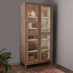 an old wooden cabinet with glass doors and shelves in the corner next to a potted plant