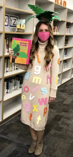 a woman wearing a pink mask and dress holding a book in front of bookshelves