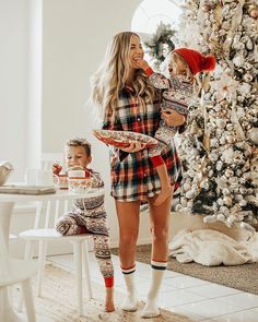 a woman holding a baby while standing next to a christmas tree