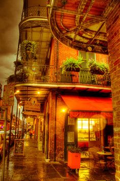 an old brick building with potted plants on the balcony and lights in the windows