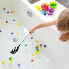 a child is playing in the bathtub with spoons and beads on it,