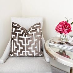 a chair with a pillow on top of it next to a table with a flower