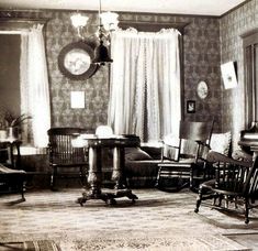 an old black and white photo of a living room with rocking chairs, a clock on the wall