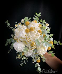 a bouquet of white and yellow flowers on a black background with greenery in the foreground