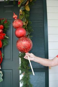 a person holding two red ornaments in front of a green door with wreaths on it