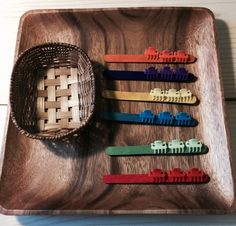 a wooden tray with six different colored hair clips on it and a woven basket in the middle