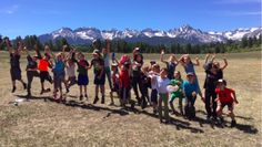 a group of people standing on top of a grass covered field with mountains in the background