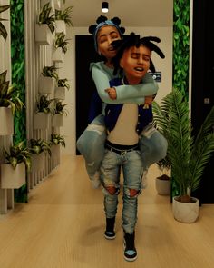 two people standing in a room with plants on the wall and one person holding another