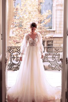 a woman is standing in an open doorway wearing a long sleeved wedding dress with sheer sleeves