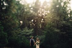 a bride and groom walking through the woods