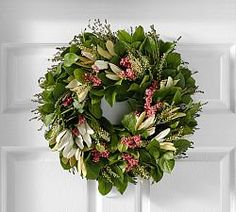 a wreath is hanging on the front door with pink flowers and greenery around it