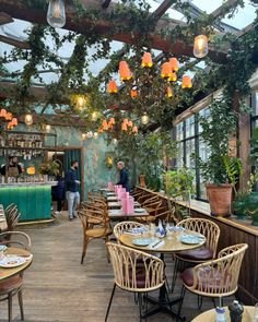 the inside of a restaurant with tables, chairs and potted plants hanging from the ceiling