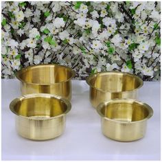 three brass bowls sitting next to each other on a white surface with flowers in the background