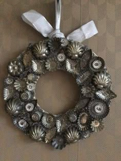 a wreath made out of seashells hanging on a wall with white ribbon and bow