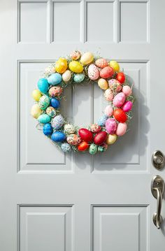 an easter wreath on the front door with colorful eggs hanging from it's side