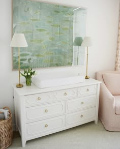 a white dresser sitting next to a pink chair in a room with a painting on the wall