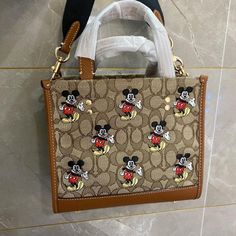 Nwt Coach Disney X Dempsey Tote 22 With Mickey Mouse Print Signature Jacquard And Refined Pebble Leather Inside Zip And Multifunction Pockets Snap Closure, Fabric Lining Handles With 4 1/4" Drop Detachable Strap With 22 1/2" Drop For Shoulder Or Crossbody Wear Four Protective Feet At Base 8 3/4" (L) X 7 3/4" (H) X 4 1/4" (W) This Coach Piece Is Crafted Of Our Signature Jacquard Made From A Blend Of Organic Cotton And Recycled Polyester Disney X Coach Disney Coach Disney Tote, Disney Coach Bags, Mickey Mouse Purse, Paw Wallpaper, Mickey Mouse Shoes, Coach Disney, Mickey Mouse Print, Disney Purse, Disney Bags