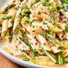 a white bowl filled with pasta and asparagus on top of a wooden table