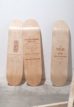 three wooden skateboards are lined up against a white wall, one has an old logo on it