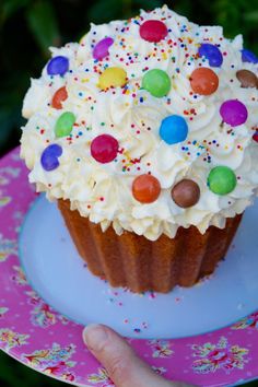 a cupcake with white frosting and multi colored candies on top, sitting on a plate