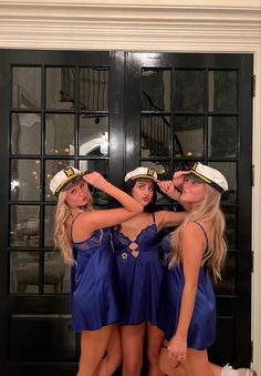 three beautiful young women standing next to each other in front of a door wearing sailor's hats