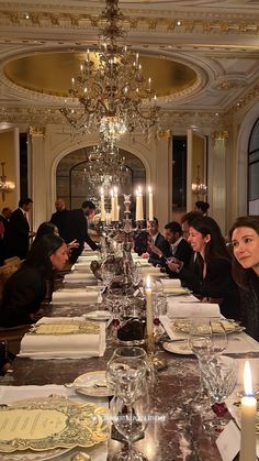 a long table with many people sitting at it and candles on the tables in front of them