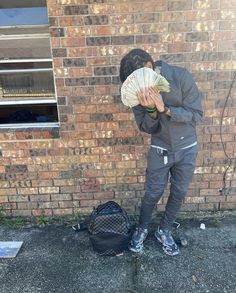 a man standing in front of a brick wall holding a bundle of money over his face