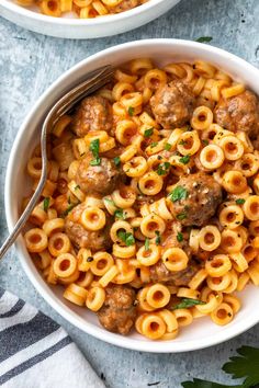 a white bowl filled with pasta and meatballs on top of a table next to a fork