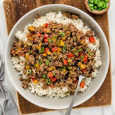 a white bowl filled with rice and ground beef on top of a wooden cutting board