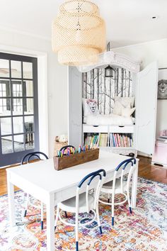 a white table with blue chairs and a book shelf in the corner on top of it