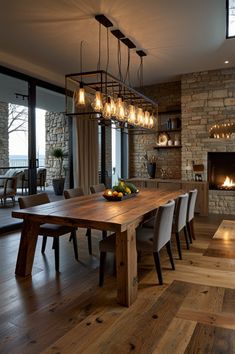 a dining room table surrounded by chairs with lights hanging from the ceiling above it and a fireplace in the background