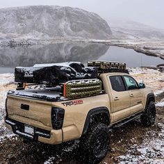 a truck parked on the side of a snow covered road next to a body of water