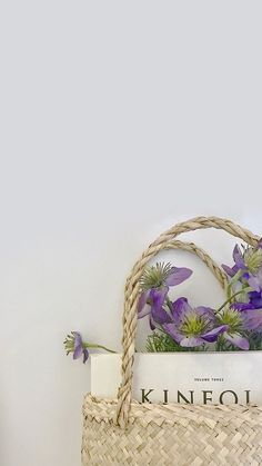 a wicker basket with purple flowers in it next to a magazine on a shelf